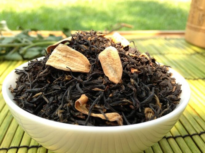 Dried tea leaves in white bowl. Grass in the background.